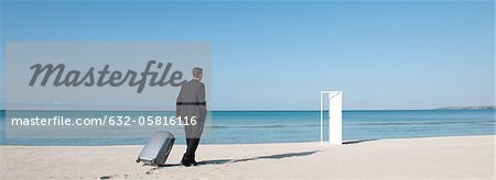 Businessman pulling suitcase on beach, walking towards half-open door
