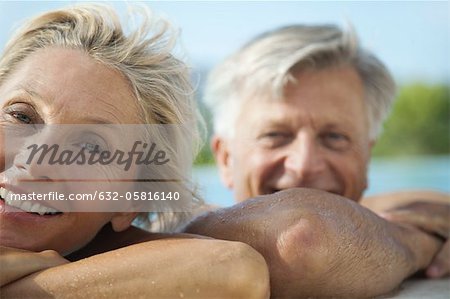 Mature couple resting their heads on side of pool, portrait