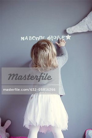 Little girl looking at words printed on wall, rear view