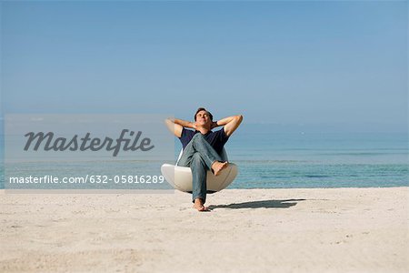 Mid-adult man relaxing in armchair on beach with eyes closed Mid-adult man relaxing in armchair on beach with eyes closed