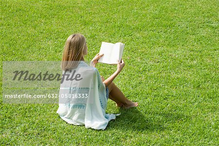 Young woman sitting on grass reading book