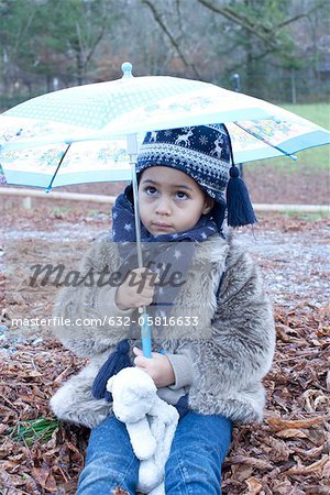 Little girl sitting under umbrella outdoors