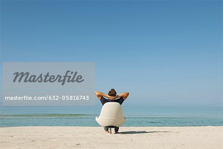 Homme assis dans le fauteuil sur la plage en regardant l'océan, vue arrière