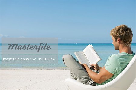 Young man reading book on beach