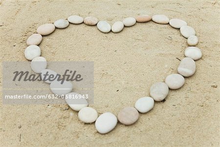 Pebbles arranged in heart shape on sand