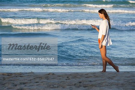 Junge Frau mit Handy, beim Spaziergang am Strand, Seitenansicht