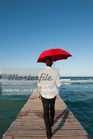 Mann zu Fuß auf Pier mit roten Regenschirm, Rückansicht
