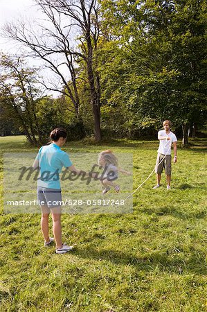 Parents and daughter skipping rope in meadow, Munich, Bavaria, Germany