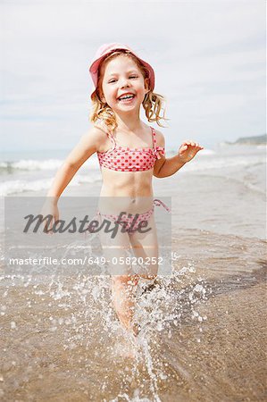 Jeune fille souriante, jouant dans les vagues sur la plage