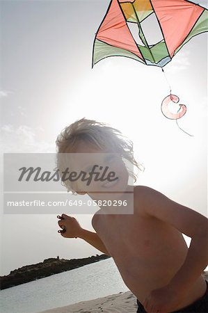 Smiling boy flying kite on beach