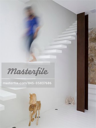 Moderne blanc salon figure floue descendant les escaliers ouverts en porte-à-faux blanc. Architectes : Hilit