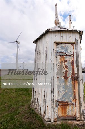 View of delapidated wooden shed with peeling paint and rusting metal door, with several wind turbines in the distance, Port of Blyth, Northumberland.