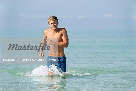 Barechested young man running in water, portrait