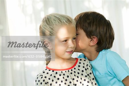 Jeune garçon whispering secret dans l'oreille de la jeune fille