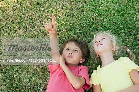 Boy and girl lying on grass, looking up and pointing