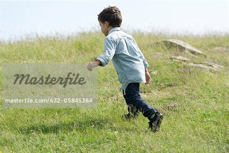 Little boy running in meadow, rear view