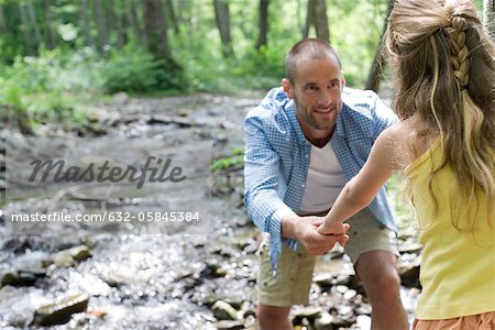 Father helping daughter crossing stream