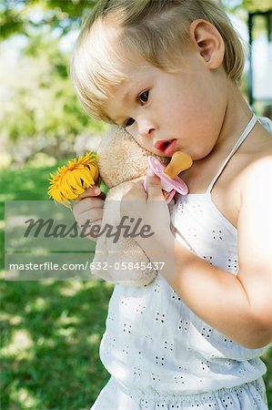 Petite fille en tenue d'ours en peluche, fleurs et suce