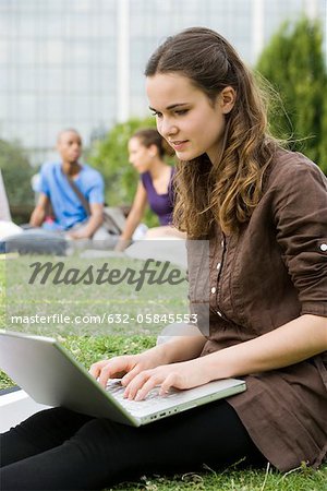 Young woman using laptop computer outdoors, people in background, portrait