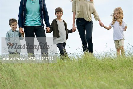 Family holding hands together outdoors, cropped