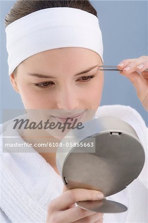 Woman plucking her eyebrow, holding a little mirror (studio)