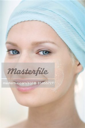 Jeune femme regardant la caméra, crème sur sa joue, close-up (studio)