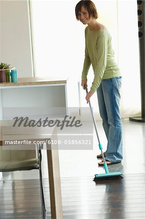 Young smiling woman sweeping living-room floor