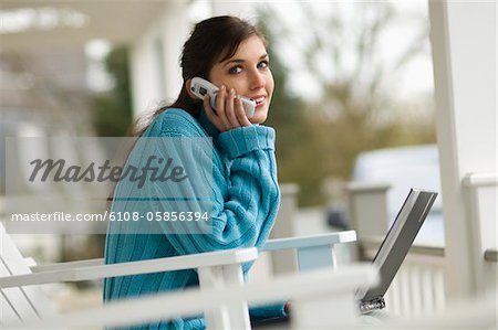 Jeune femme à l'aide de téléphone portable, assis sur une chaise, en regardant la caméra, à l'extérieur