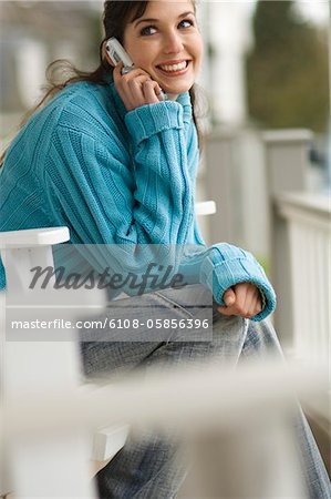 Lächelnde Frau mit Handy, sitzend auf einem Stuhl im freien