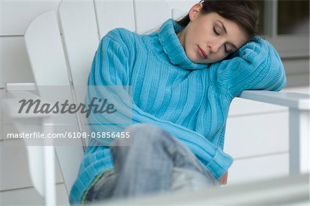 Jeune femme avec le pull bleu, dormir sur une chaise posé sa tête sur son bras, à l'extérieur