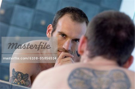 Homme tatoué, torse, en face du miroir de salle de bains