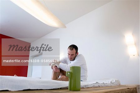 Man listening to iPod player, sitting on a bed
