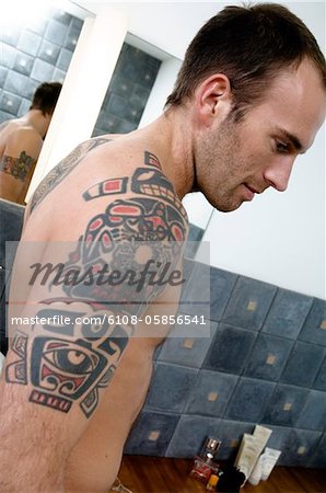 Tattooed man, barechested, standing in the bathroom, in profile