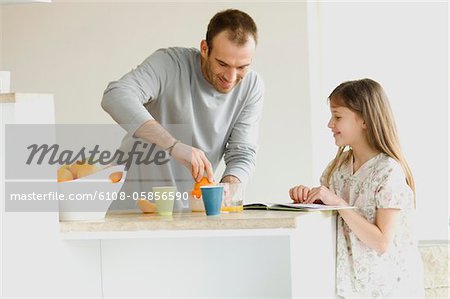 Little girl watching man squeezing oranges in the kitchen