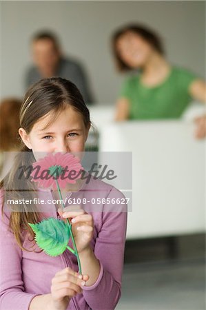 Petite fille tenant une fleur en plastique devant son visage, couple en arrière-plan