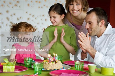 Couple and 2 little girls with birthday cake at lunch table