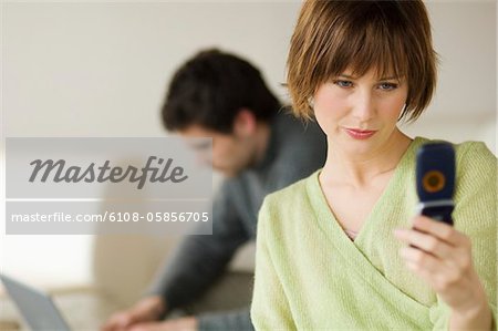 Woman using mobile phone, man using laptop computer in the background