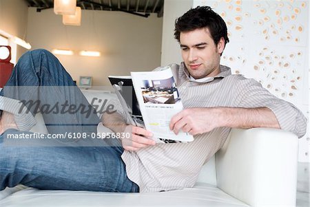 Mann, liegend auf einem Sofa, Magazin lesen