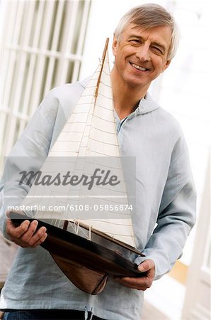 Smiling senior man holding a model boat outdoors