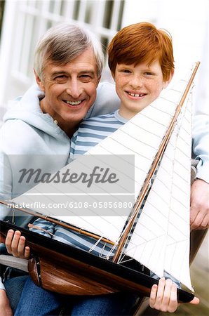 Senior man and boy holding a model boat, outdoors