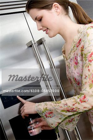 Young woman pouring water from a refrigerator water dispenser into a glass