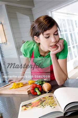 Young woman looking at recipe book, vegetables on a chopping board