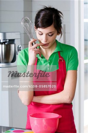 Femme jeune pensée dans la cuisine, tenant un fouet