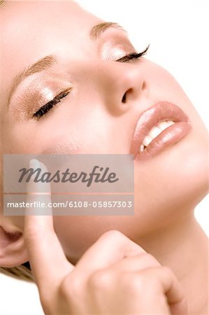 Woman putting make-up base on her cheek, shut eyes, indoors (studio)