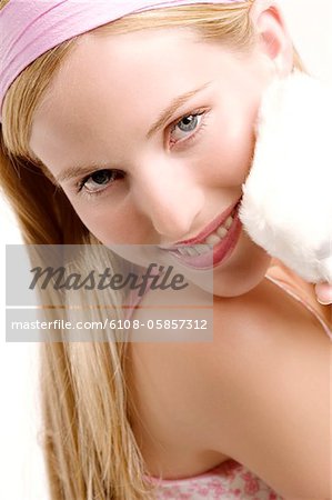 Portrait d'une jeune femme tenant une houppette sur sa joue, à l'intérieur (studio)