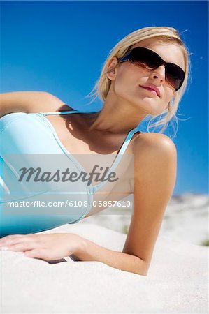 Young woman in swimming costume lying on the beach, sunglasses