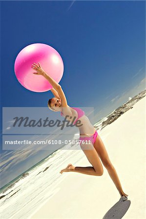 Jeune femme souriante en bikini rose sur la plage, une grosse boule de levage