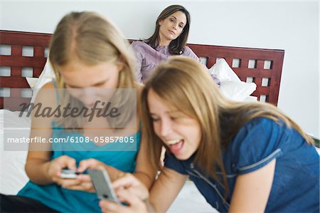 2 smiling teenage girls using mobile phones, woman in background