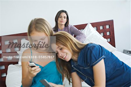 2 smiling teenage girls using mobile phones, woman in background