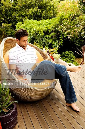 Young man sitting in armchair reading a book, outdoors